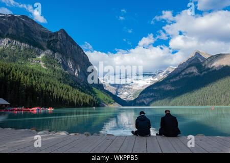 Zwei Menschen sitzen und den wunderschönen Lake Louise und Berge bei Banff, Kanada genießen Stockfoto