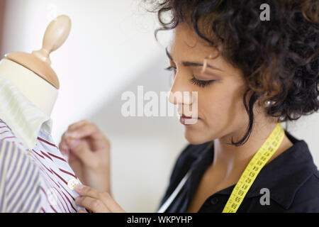 Junge hispanic weibliche Schneiderin Nähen Taste auf Schneiderei Mannequin-Shirt. Stockfoto