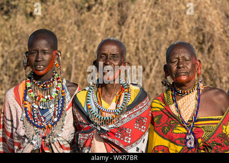 Drei Maasai Frauen tragen traditionelle Kangas und Schmuck, Halsketten, Ohrringe Singen in einem Dorf in der Nähe der Masai Mara, Kenia, Ostafrika Stockfoto