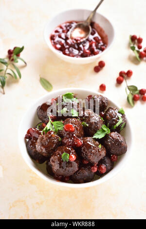 Lecker Frikadellen mit Preiselbeersoße in Weiß Schüssel auf hellem Stein Hintergrund. Geschmorte Hackfleischbällchen in süßen Beeren-Sauce. Stockfoto