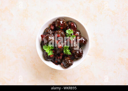 Nahaufnahme von Frikadellen mit Preiselbeersoße in Weiß Schüssel auf hellem Stein Hintergrund mit Freier Text. Geschmorte Hackfleischbällchen in süßen Beeren-Sauce. Top vi. Stockfoto