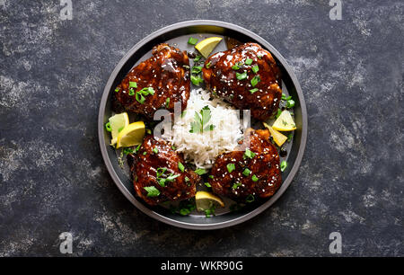 Gebackene Hühnerkeule mit Reis über dunklen steinernen Tisch. Gegrilltes Hähnchen Schenkel in Honig Sojasauce. Lecker essen im asiatischen Stil. Ansicht von oben, flach Stockfoto