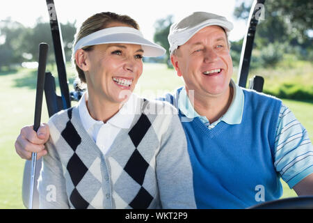 Viel Spaß paar im Golf Buggy lächelnd an einem sonnigen Tag auf dem Golfplatz sitzen Stockfoto