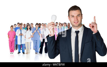 Das zusammengesetzte Bild im Geschäftsmann holding Glühbirne und nach gegen die Gruppe der Arbeitnehmer Stockfoto