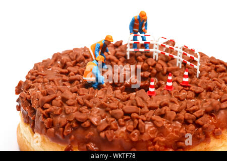 Konzeptionelle Bild einer Miniatur Abbildung Arbeiter auf einer Schokolade donut Blick nach unten das Loch in der Mitte stand Stockfoto