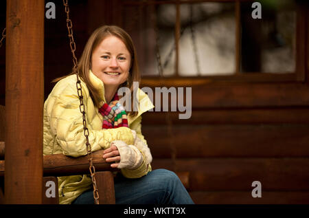 Junge Frau sitzt auf einer Hängematte Stuhl auf dem Stoop von einem Blockhaus. Stockfoto
