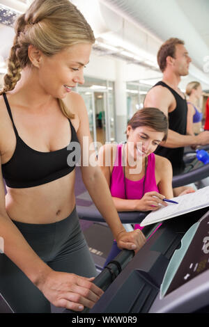 Trainer im Gespräch mit Ihren Kunden auf dem Laufband im Fitnessstudio Stockfoto