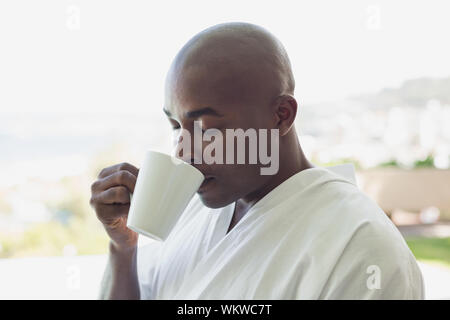 Schöner Mann im Bademantel trinken Kaffee draußen an einem sonnigen Tag Stockfoto