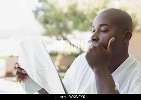Schöner Mann im Bademantel lesen Zeitung außerhalb an einem sonnigen Tag Stockfoto