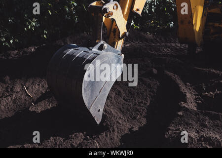 Gelber bagger Schaufel graben ein Loch in den schwarzen Boden an einem sonnigen Tag. Bau Maschinen während der Arbeit. Stockfoto