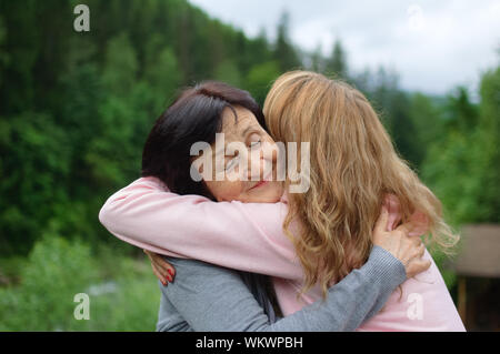Mutter und ihre erwachsene Tochter sind umarmen Ausgabe Zeit zusammen im Freien über Landschaft aus Wald und Berge. Konzept der Zärtlichkeit, Pflege, Familie Stockfoto