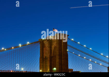 In der Nähe der Pfeiler der Brooklyn Bridge mit Fahne in der Nacht, New York City, USA Stockfoto