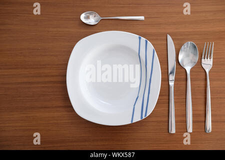 Weißes Porzellan Geschirr mit hellen Metall Besteck und Serviette auf einem Holztisch. Stockfoto