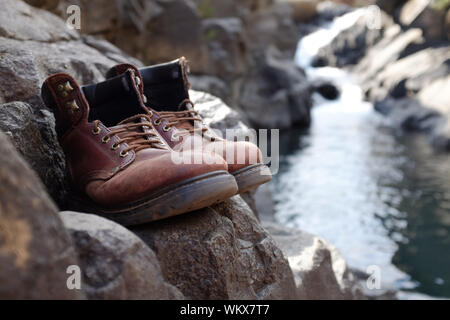 Begrenzte Fokus Wanderschuhe auf Rock mit unscharfen Fluss, Bach, Wasserfall bei Lotheni. KwaZulu-Natal im Südafrikanischen Drakensburg Berge Stockfoto