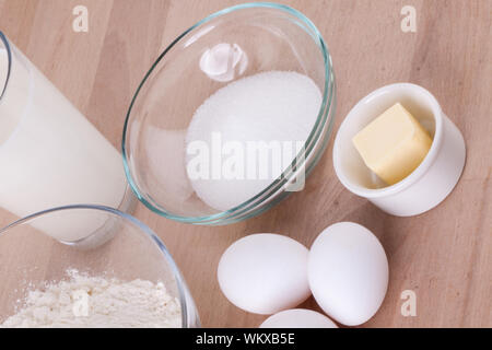 Zutaten in der Küche mit einer Schüssel Mehl, Eier, Zucker, Krug mit Milch und Butter bereit, einen Kuchen backen oder Teig backen Stockfoto