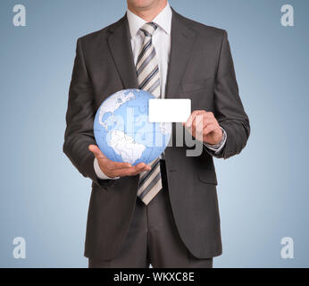 Geschäftsmann in Anzug halten leere Karte und Globus, bestehend aus Rätsel. Blauer Hintergrund Stockfoto