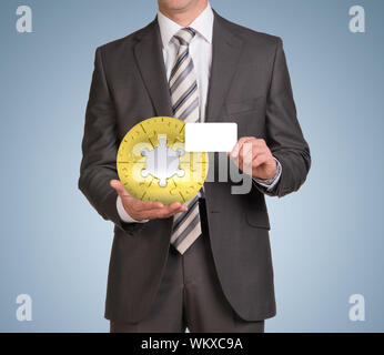 Geschäftsmann in Anzug halten leere Karte und Puzzle Kugel. Blauer Hintergrund Stockfoto