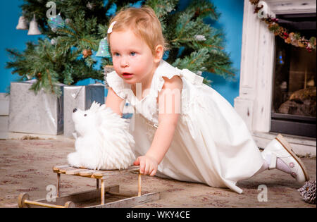 Kleines Mädchen in einem festlichen Kleid spielt in der Nähe von the Christmas tree Stockfoto