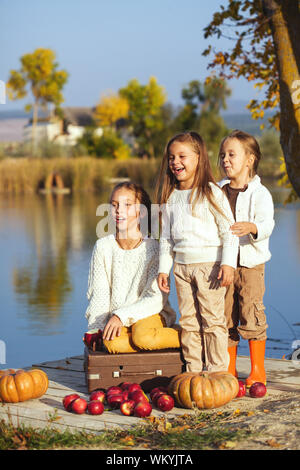 Drei fröhliche kleine Mädchen, die auf dem See im warmen Herbst Tag/Herbst lifestyle Portrait von Kindern Spaß auf hölzernen bearth über den Fluss La Stockfoto