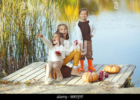 Drei fröhliche kleine Mädchen, die auf dem See im warmen Herbst Tag/Herbst lifestyle Portrait von Kindern Spaß auf hölzernen bearth über den Fluss La Stockfoto