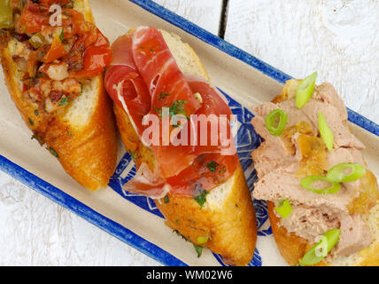 Tapas Bruschetta mit Speck, gebratenes Gemüse, Schinken und Pastete mit Frühlingszwiebeln auf Knoblauchbrot auf weißem Holz- Hintergrund. Ansicht von oben Stockfoto