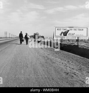 Ansicht der Rückseite zwei Männer zu Fuß in Richtung Los Angeles, Kalifornien, USA, auf der Piste in der Nähe von Billboard, dass der sagt: "Nächstes Mal den Zug versuchen. Entspannen.', Dorothea Lange, U.S. Farm Security Administration, März 1937 Stockfoto