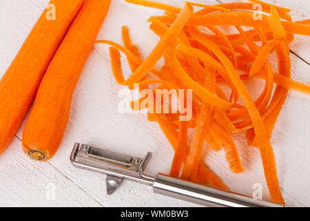Frische geschälte Karotten in Scheiben geschnitten in dünne Stäbe für Karotten Julienne mit einem Cutter Metall Küche auf weißem Hintergrund Stockfoto