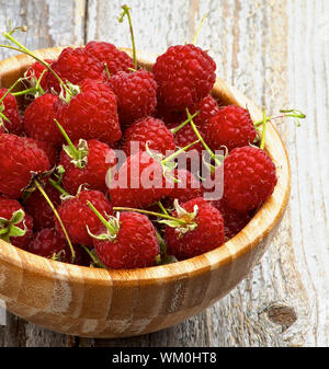 Perfekte Reife Himbeeren mit Stängel in Houten Querschnitt auf rustikalen Holzmöbeln Hintergrund Stockfoto