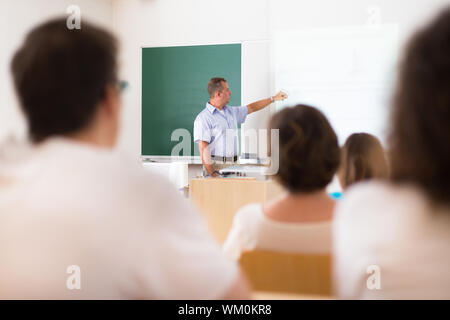 Lehrer an der Universität vor einem Whiteboard-Bildschirm. Schüler hören um zu belehren und sich Notizen macht. Stockfoto