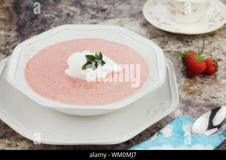 Eine Schüssel mit gekühlten Erdbeer-Suppe, garniert mit einem Klacks Schlagsahne und einen frischen Zweig Schokolade Minze. Stockfoto