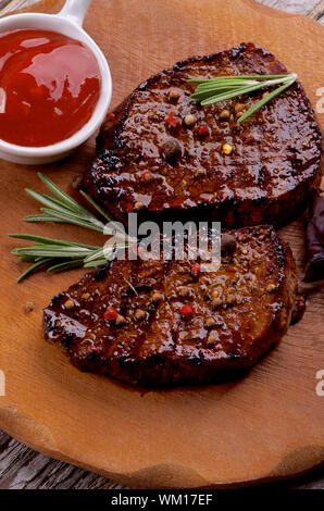 Lecker gebratene Rindersteaks mit Gewürzen und Tomatensauce closeup auf Holzplatte Stockfoto