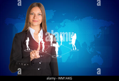 Schöne Geschäftsfrau im Anzug drückt mit dem Finger auf virtuellen Button. Weltkarte und Business Silhouetten im Hintergrund Stockfoto