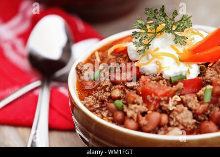 Schüssel mit Chili Con Carne mit Sauerrahm, Schnittlauch und Cheddar Käse garniert. Extrem flache Tiefenschärfe mit selektiven Fokus in der Mitte der Schüssel. Stockfoto