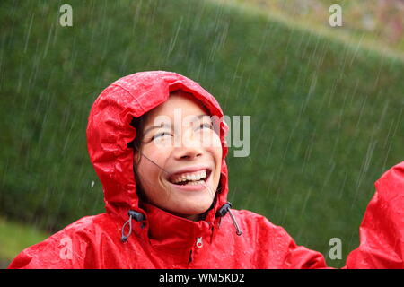 Junge Frau trägt eine rote Regenjacke genießen den Regen und Spaß außerhalb. Stockfoto