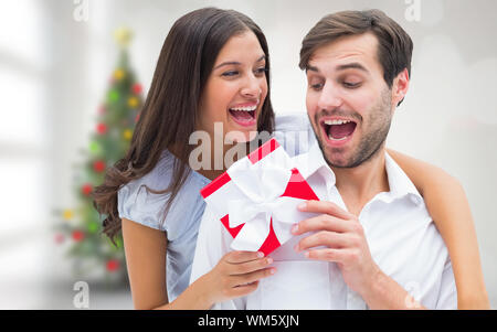 Frau überraschend Freund mit Geschenk gegen blurry Christbaum im Zimmer Stockfoto