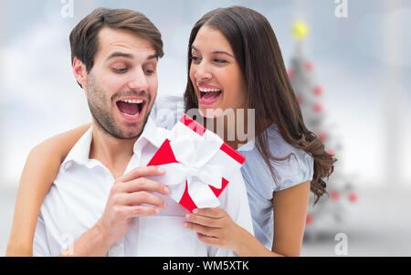 Frau überraschend Freund mit Geschenk gegen blurry Christbaum im Zimmer Stockfoto