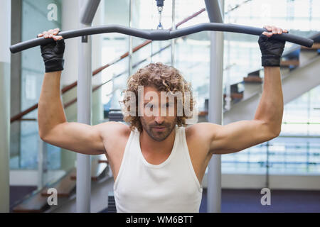 Porträt von einem gutaussehenden jungen Mann Ausübung auf einem lat Maschine in der Turnhalle Stockfoto