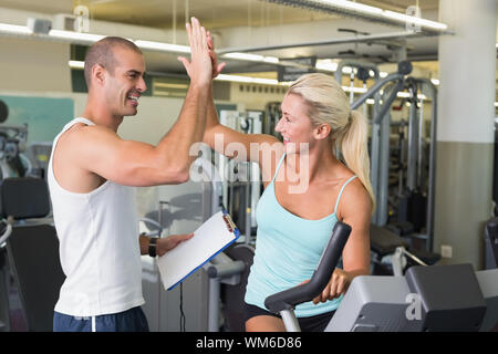 Lächelnd männlichen Trainer hohe fünf zu seinen Client auf dem Fahrrad im Fitnessstudio Stockfoto