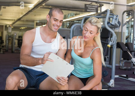 Schöne junge Frau, die ihre Leistung diskutieren über die Zwischenablage mit einem Trainer im Fitnessstudio Stockfoto