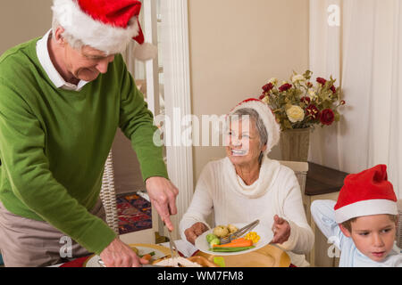 Großvater in santa hut mit gebratenem Truthahn zu Weihnachten zu Hause im Wohnzimmer Stockfoto