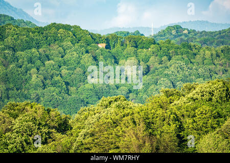 Grüne Hügel mit einem einsamen Haus und hohe Berge am Horizont. Grüne Tal mit dörfliche Siedlungen im Licht des Sonnenuntergangs. Stockfoto