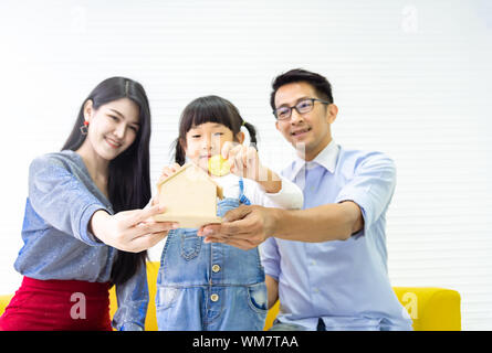 Hände halten Sparschwein. Familie Sparen von Geld für Holz Bank. Hübsches kleines Mädchen und Familie setzenden Münzen in Bank für Traumhaus. Kinder, mo Stockfoto