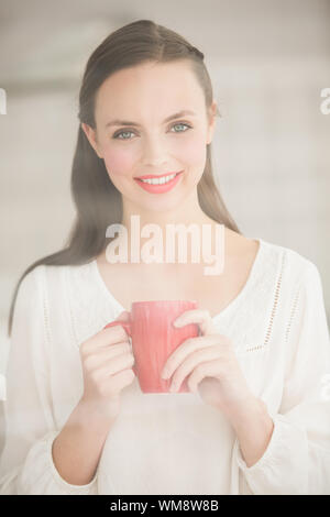 Hübsche Brünette mit einem Becher zu Hause im Wohnzimmer Stockfoto