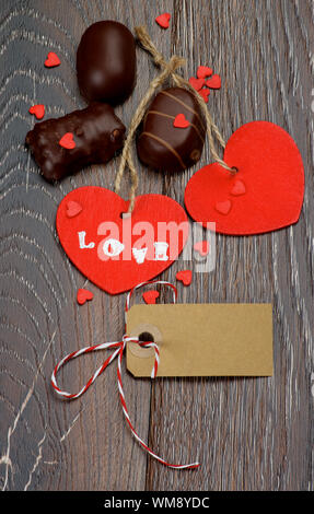 Zwei rote Herzen mit dem Wort Liebe, leere Karte und Pralinen closeup auf dunklem Hintergrund Stockfoto
