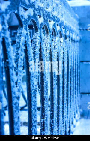 Nahaufnahme des gefrorenen schwarzes Eisenzaun und großen Frost drauf. Blaue Farben. Stockfoto