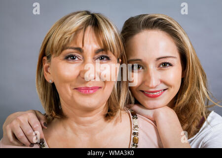 Verspielte schöne junge Mutter und ihre Tochter zusammen mit dem jungen Mädchen peeking Out an der Seite mit einem glücklichen Grinsen posieren, auf einem g isoliert Stockfoto