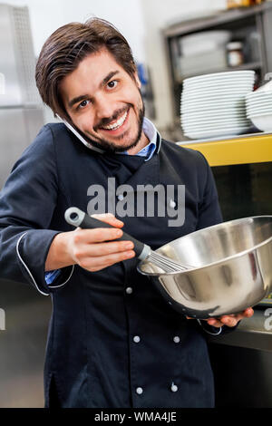 Professionelle Koch oder Küchenchef in Uniform mit einem Edelstahl Schüssel in der Hand, einen Anruf auf seinem Smartphone während das Abendessen vorbereiten Stockfoto