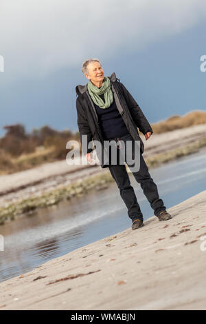 Gerne ältere Frau Herumtollen am Strand schreiten zusammen mit ausgebreiteten Armen und einem Lächeln der Anerkennung, die sie genießt die Natur und die Freiheit ihrer Stockfoto