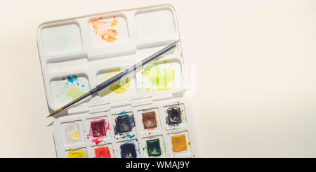 Mehrfarbige Aquarellfarbe aus weißem Kunststoff mit Bürste liegt auf strukturierte Zeichenpapier, Flach, kopieren. Stockfoto