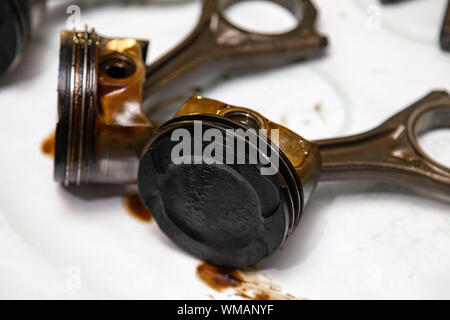 Zwei Metall auto Kolben in schlechtem Zustand mit Ruß Öl entfernt aus gebrauchten Motor in eine Anzahlung von Öl liegen auf der Workbench in einem Fahrzeug Reparaturwerkstatt für war Stockfoto